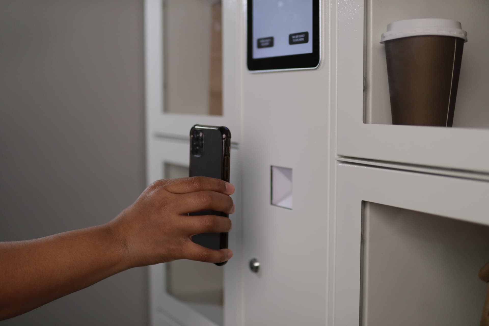 Customer holding a phone at a Lavii smart food locker, with an open compartment and a prepared order inside